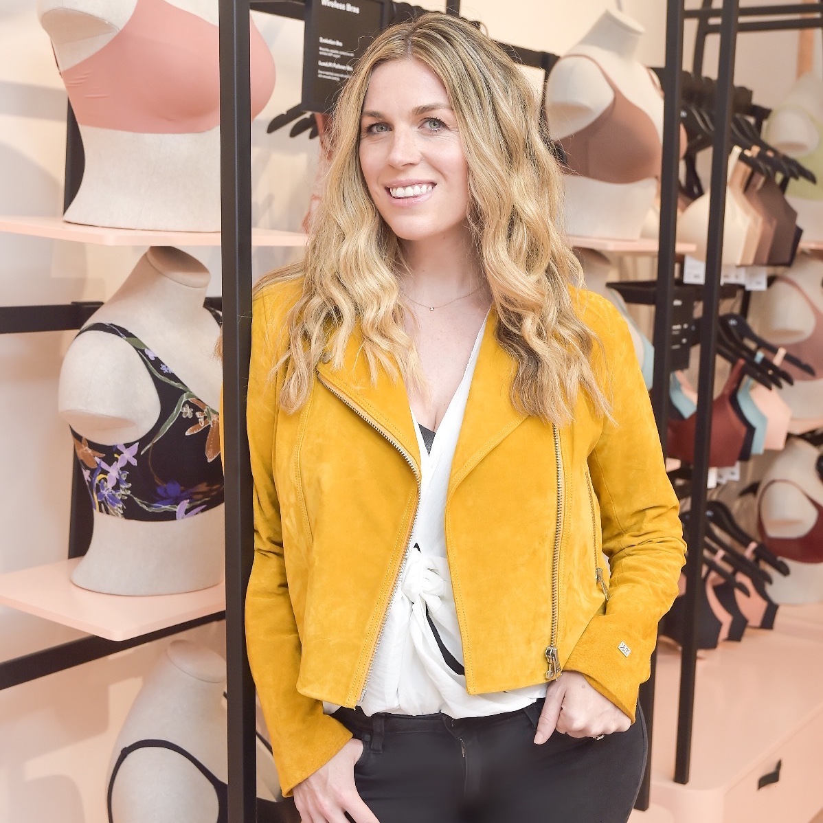 CEO of Knix Joanna Griffiths stands in front of a shelf holding mannequin torsos that display Knix bras.