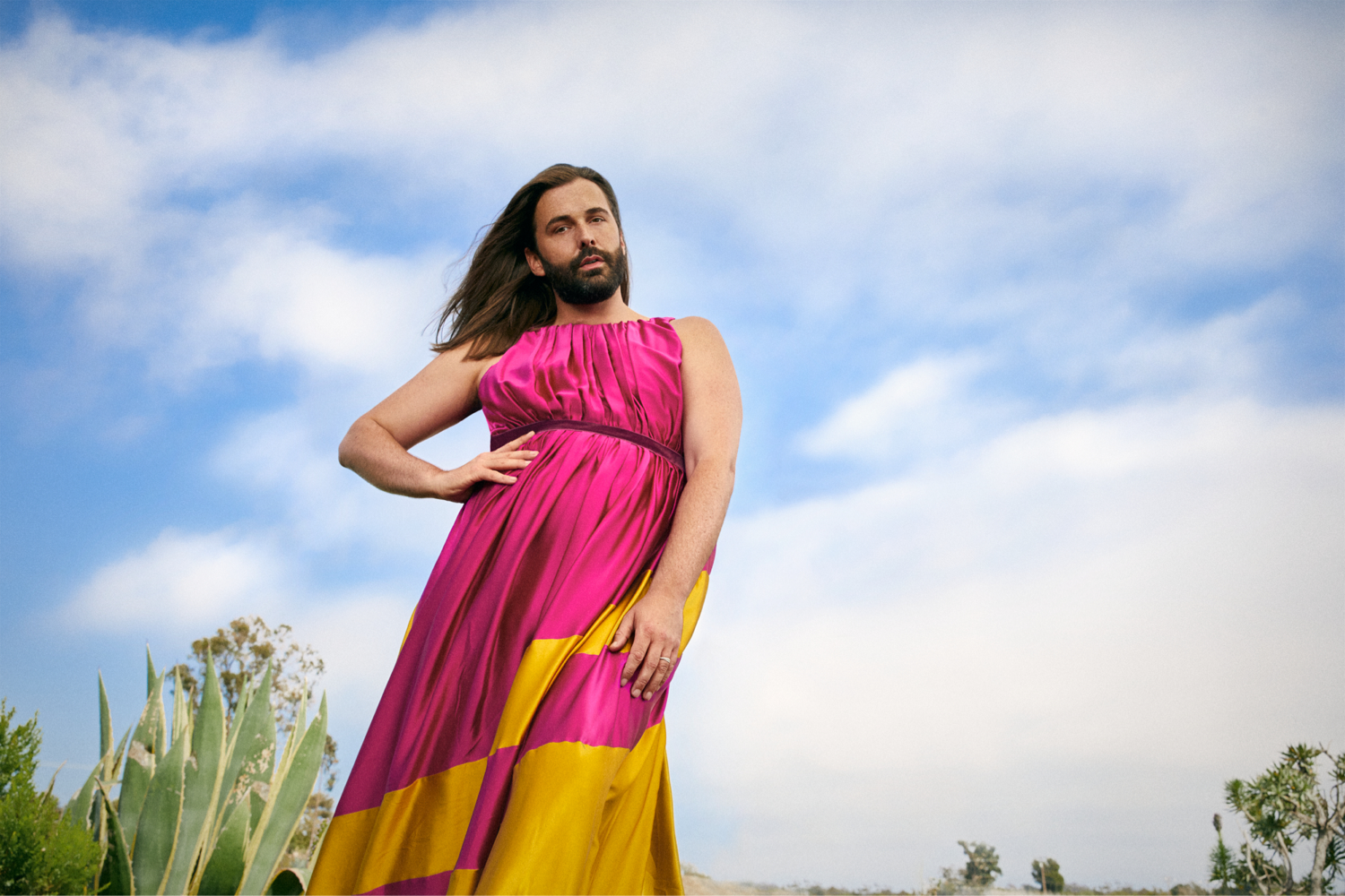 Jonathan Van Ness wearing a pink and yellow dress against a blue sky backdrop