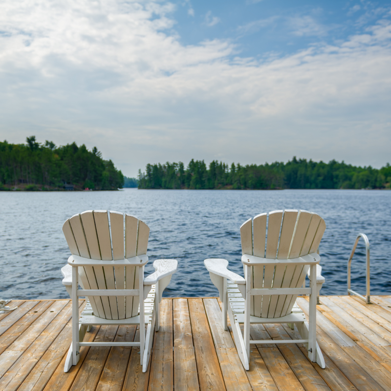 Two chairs on a deck sitting by the lake. 