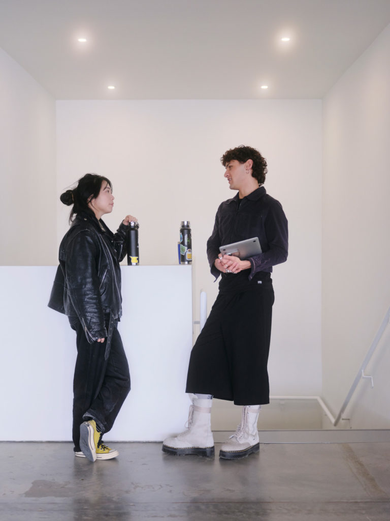 Two workers standing in the hallway wearing black and talking to each other at SSENSE's Montreal office