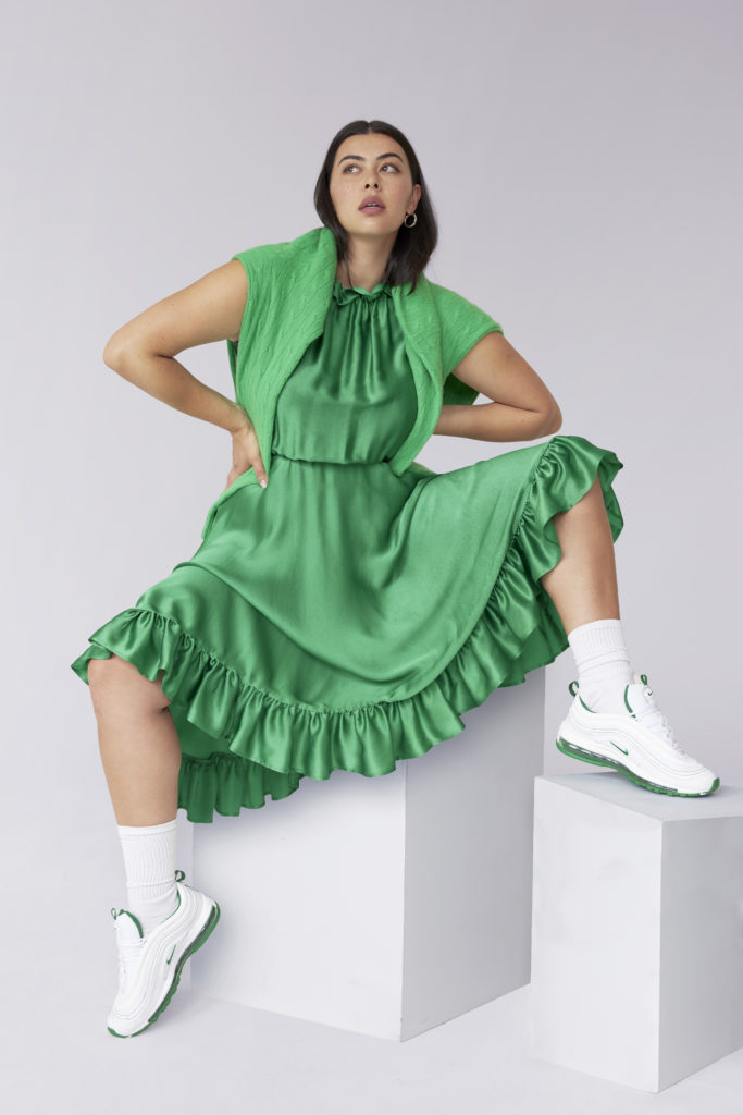 Model Lauren Chan sitting on a white block wearing a green dress and white sneakers