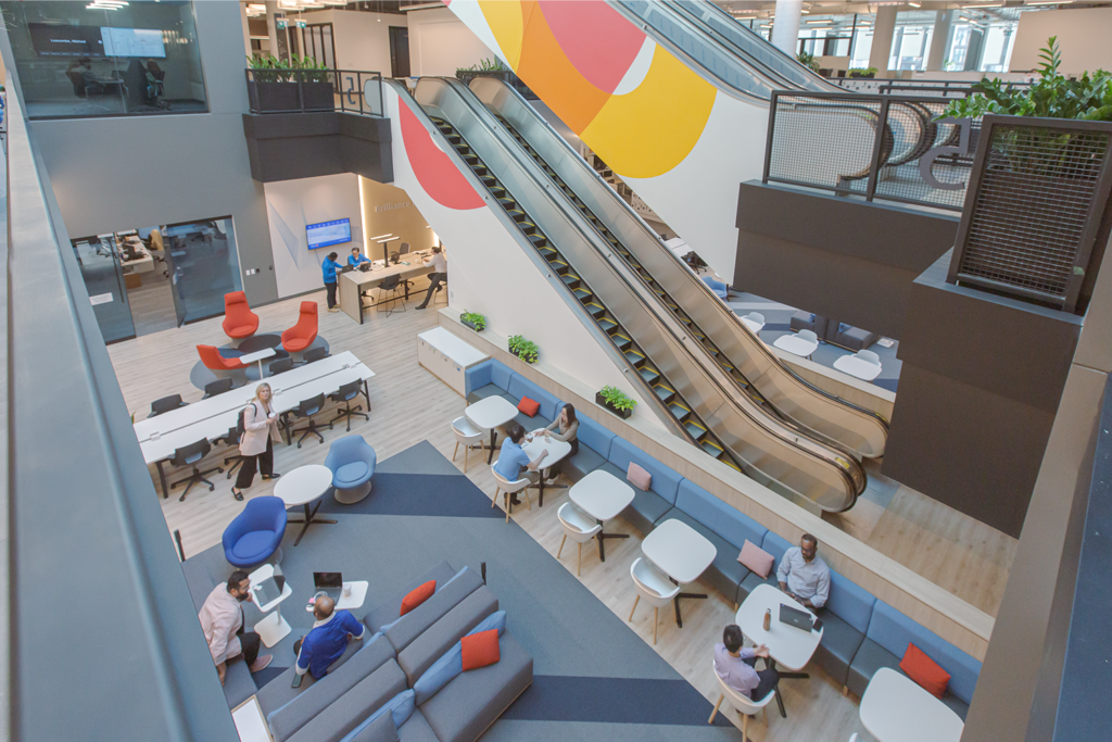 Escalators inside the atrium area of BMO's Toronto office with people sitting at chairs and tables