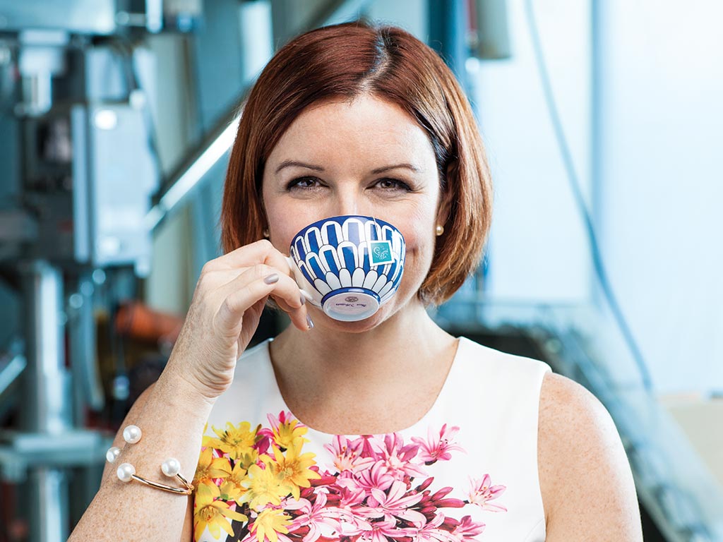 A woman in a floral shirt sips from a blue patterned tea cup.