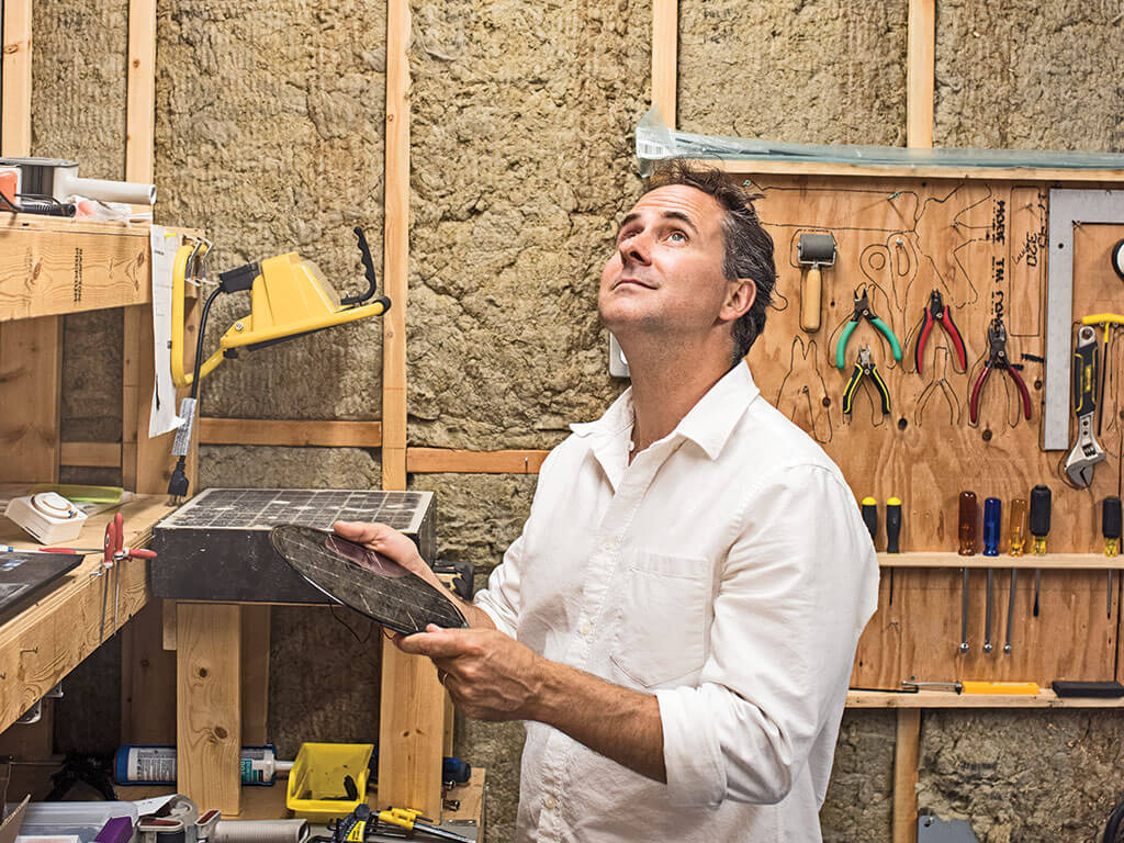 A man standing in a workshop looks up at the ceiling while holding a flat round object.
