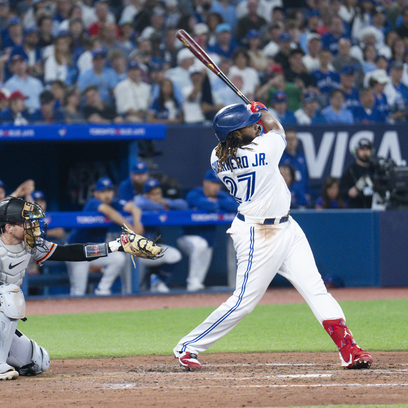 A baseball player swinging a bat wearing a Toronto Blue Jays uniform 