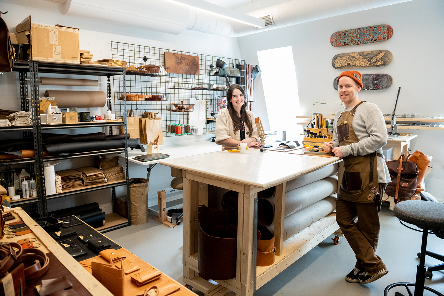 Two people standing inside their leather-making studio smiling and leaning on a table