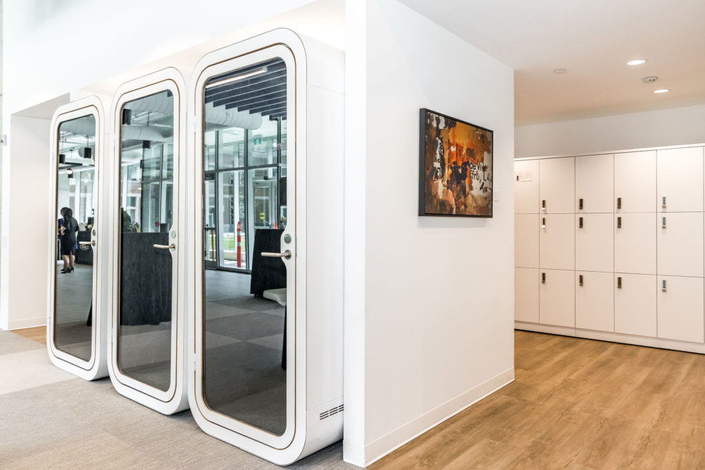 A white row of private phone booths inside an office space next to a row of white lockers