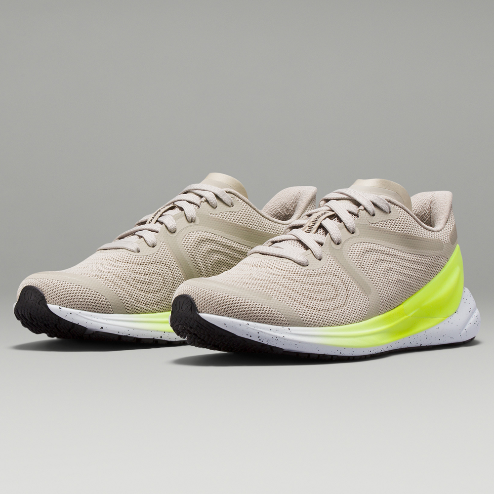 A pair of beige sneakers with a lime green block on the side on a grey background