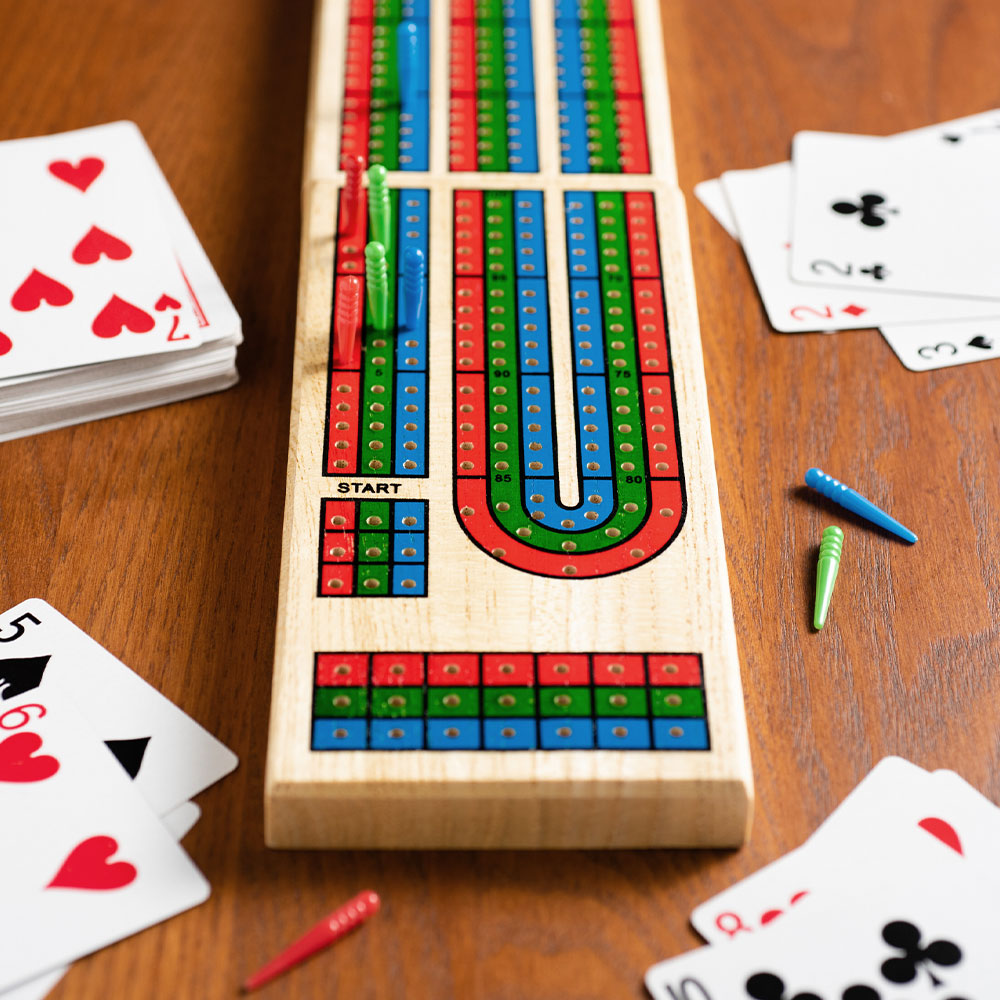 A cribbage board with red blue and green pegs surrounded by playing cards