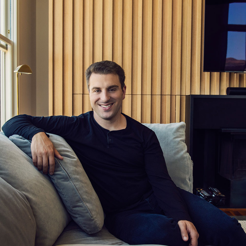 Brian Chesky, CEO of Airbnb, sits on a grey sofa